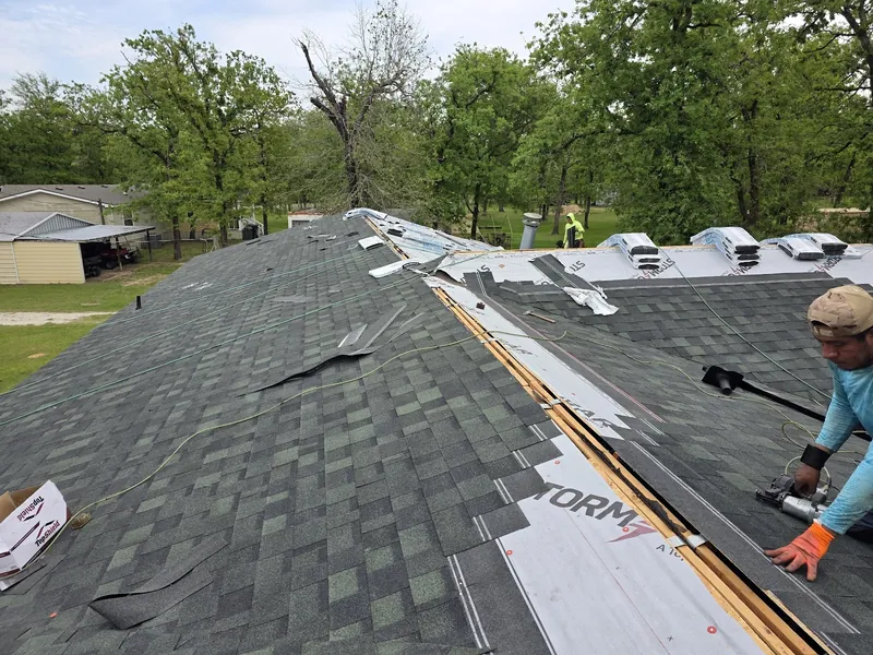 Roofer installing new shingles beside the ridge vents on a home surrounded by oak trees