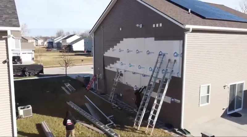 Crew installing new lap siding on a two-story home, with house wrap showing and ladders against the wall