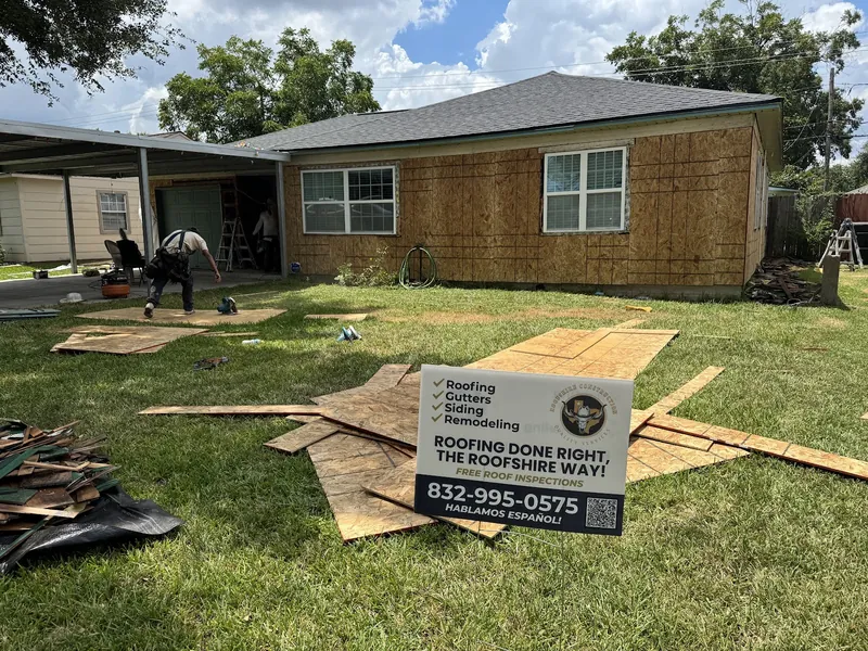 Single-story home with the old siding stripped to the sheathing and a Roofshire Construction yard sign in the lawn